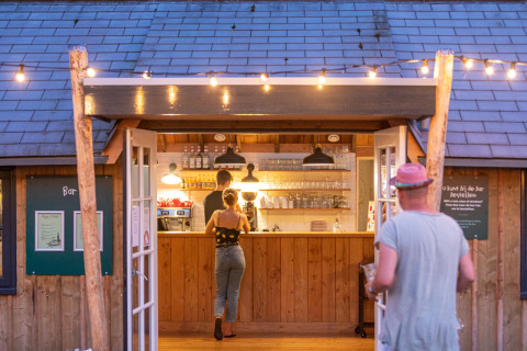 Personas piden bebidas en un bar de madera acogedor con luces en Huttopia De Roos, Overijssel, Países Bajos.