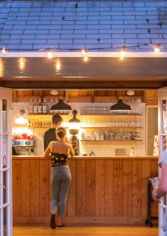 Personas piden bebidas en un bar de madera acogedor con luces en Huttopia De Roos, Overijssel, Países Bajos.