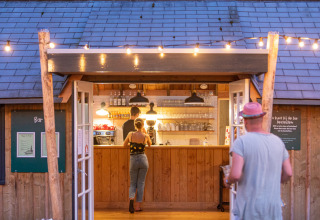 Persone ordinano da bere al bar in legno illuminato al parco vacanze Huttopia De Roos, Overijssel, Paesi Bassi.