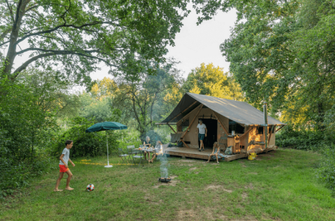 Familia acampando en Huttopia De Veluwe, Gelderland, Países Bajos, con una tienda grande y naturaleza verde.