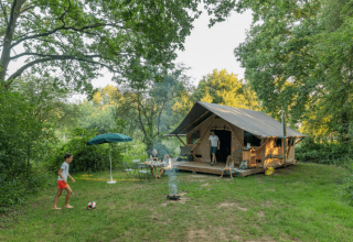 Familie kampeert bij Huttopia De Veluwe in Gelderland, Nederland, met grote tent en groene omgeving.