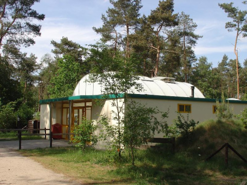 Camping Huttopia De Veluwe en Gelderland, Países Bajos, edificio moderno rodeado de naturaleza y árboles.