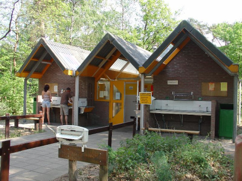 Edificio de servicio con lavabos y personas en Camping Huttopia De Veluwe, parque vacacional en Gelderland, Países Bajos.