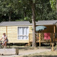 Kvinde cykler foran en Mobile home Cottage i skov, terrasse med parasol og håndklæder i solen.