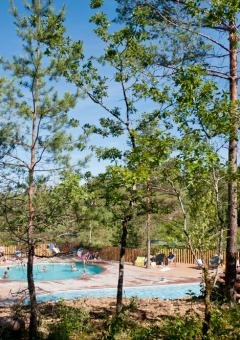 Piscina al aire libre rodeada de árboles en Village Huttopia Lanmary, parque vacacional en Nouvelle-Aquitaine, Francia.