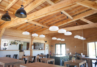 Lyse, træbeklædte spiseområde med moderne lamper i Village Huttopia Lanmary, Nouvelle-Aquitaine, Frankrig.