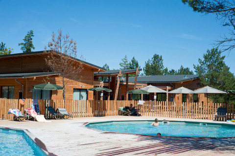 Piscina al aire libre y cabañas de madera en Village Huttopia Lanmary, parque vacacional en Nouvelle-Aquitaine, Francia.