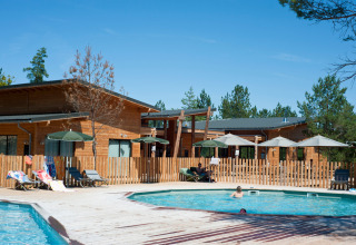 Udendørs swimmingpool og træhytter i Village Huttopia Lanmary, feriepark i Nouvelle-Aquitaine, Frankrig.