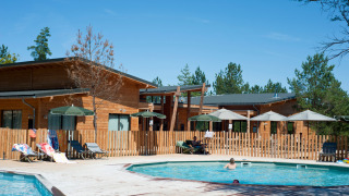 Piscina al aire libre y cabañas de madera en Village Huttopia Lanmary, parque vacacional en Nouvelle-Aquitaine, Francia.