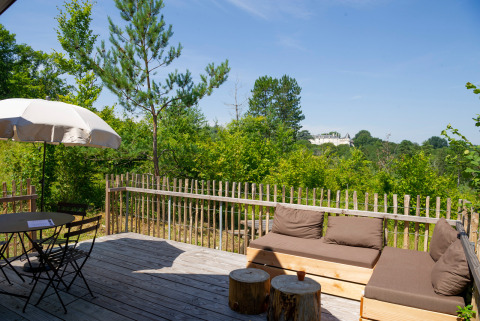 Terraza de madera con asientos y sombrilla, vista al bosque en Village Huttopia Lanmary, Nouvelle-Aquitaine, Francia.