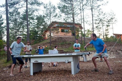 Vakantiegangers spelen buiten tafeltennis tussen de bomen in Village Huttopia Lanmary, Nouvelle-Aquitaine, Frankrijk.