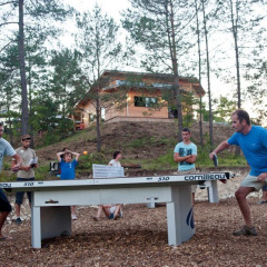 Vacacionistas juegan al ping-pong al aire libre entre árboles en Village Huttopia Lanmary, Nouvelle-Aquitaine, Francia.