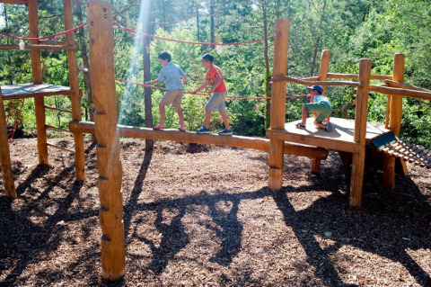 Kinderen spelen op een houten speeltuin in Village Huttopia Lanmary, vakantiepark in Nouvelle-Aquitaine, Frankrijk.