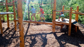 Niños jugando en un parque infantil de madera en Village Huttopia Lanmary, Nueva Aquitania, Francia.