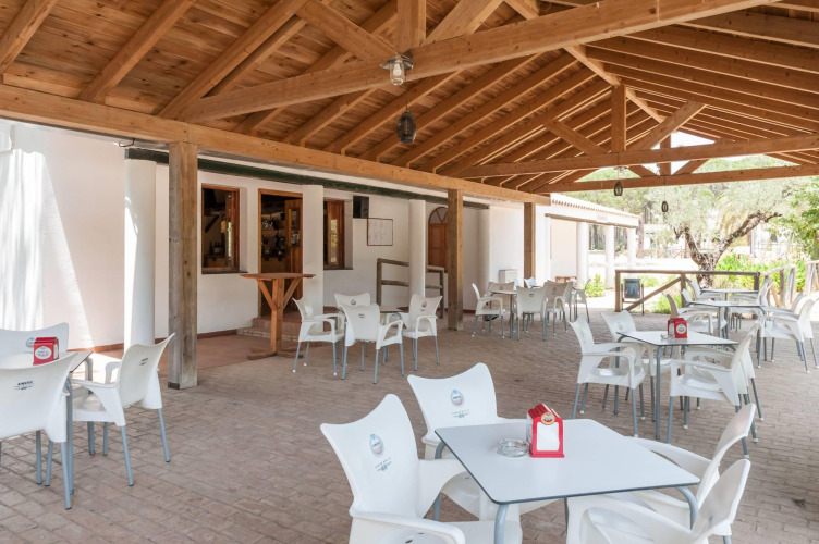 Überdachte Terrasse mit weißen Stühlen und Tischen im Ferienpark Huttopia Parque de Doñana, Andalusien, Spanien.