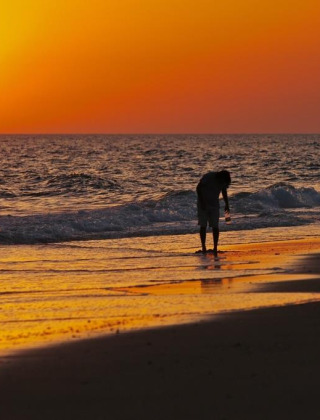 Dos personas recogen conchas al atardecer en la playa cerca de Hinojos, Andalucía, bajo un cielo anaranjado.