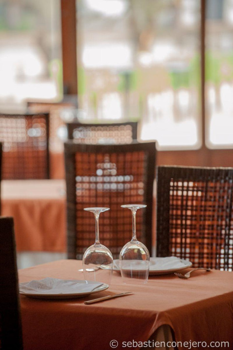 Mesa para dos personas en restaurante de Huttopia Parque de Doñana, Andalucía, España, con luz natural al fondo.