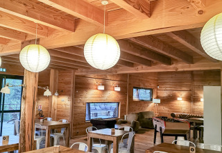 Area comune accogliente con tavoli in legno e sedie bianche al Village Huttopia Sud-Ardèche, Auvergne-Rhône-Alpes, Francia.