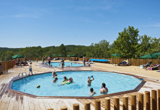 Piscine all'aperto con ospiti, terrazza in legno e ombrelloni verdi al Village Huttopia Sud-Ardèche, Francia.