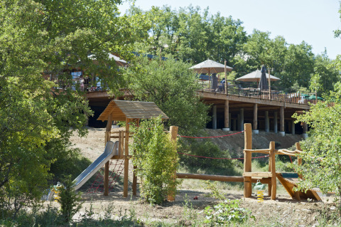 Parque infantil al aire libre y terraza de madera con sombrillas en un complejo vacacional en Francia.