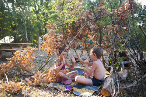 Dos niños juegan juntos dentro de una cabaña improvisada hecha de ramas en Village Huttopia Sud-Ardèche, Francia.
