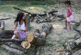 Deux filles jouent parmi des bûches au Village Huttopia Sud-Ardèche, parc de vacances en Auvergne-Rhône-Alpes, France.