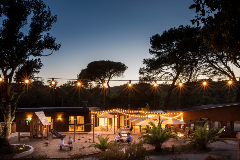 Aftenbillede af Huttopia La Forêt de Janas feriepark i Provence-Alpes-Côte d’Azur med lyskæder og legeplads.