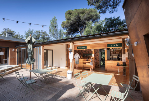 Zona de comedor al aire libre en Huttopia La Forêt de Janas, con mesas y bar en Provence-Alpes-Côte d’Azur, Francia.