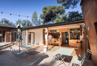 Outdoor dining area with tables and bar at Huttopia La Forêt de Janas in Provence-Alpes-Côte d’Azur, France.