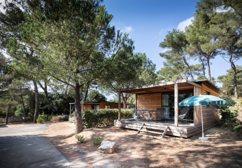 Cabaña de madera con terraza y sombrilla en Huttopia La Forêt de Janas, parque vacacional en Provenza, Francia