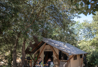 Famiglia che si rilassa davanti a una tenda safari tra gli alberi a Huttopia La Forêt de Janas, Francia.