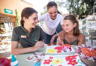Drie personen knutselen en schilderen bloemrijke kunst buiten bij Huttopia La Forêt de Janas vakantiepark.