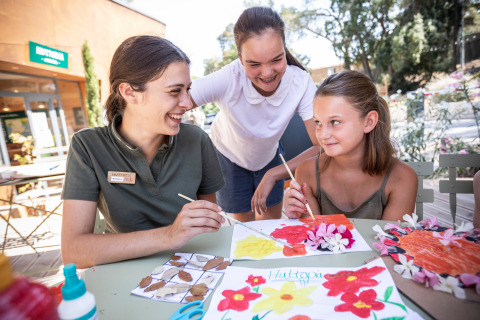 Tres personas pintan y crean manualidades florales al aire libre en Huttopia La Forêt de Janas, Francia.