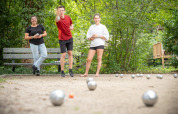 Drei junge Erwachsene spielen Boule in einem grünen Ferienpark bei Village Huttopia Pays de Condrieu, Frankreich.