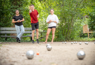 Tre unge voksne spiller petanque i en grøn naturpark ved Village Huttopia Pays de Condrieu i Frankrig.