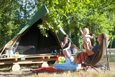 Familia disfrutando del camping frente a una tienda tipi Bonaventure en Village Huttopia Lac de Rillé, Francia.
