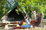 Familia disfrutando del camping frente a una tienda tipi Bonaventure en Village Huttopia Lac de Rillé, Francia.