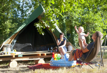 Familia disfrutando del camping frente a una tienda tipi Bonaventure en Village Huttopia Lac de Rillé, Francia.