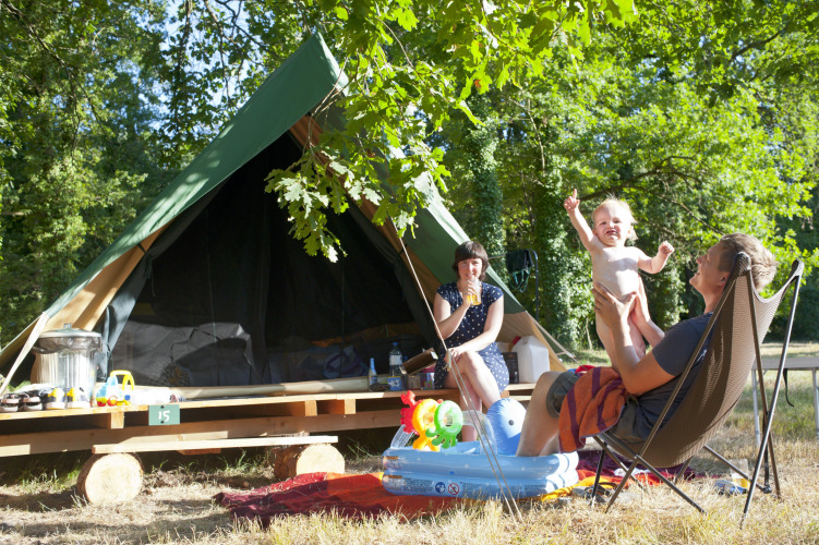Familia disfrutando del camping frente a una tienda tipi Bonaventure en Village Huttopia Lac de Rillé, Francia.