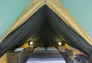 Vista interior de una tienda tipi acogedora con cama doble y mesitas en Village Huttopia Lac de Rillé, Francia.