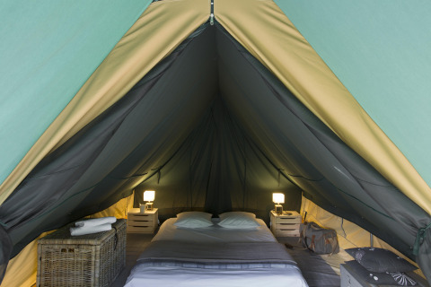 Vista interior de una tienda tipi acogedora con cama doble y mesitas en Village Huttopia Lac de Rillé, Francia.