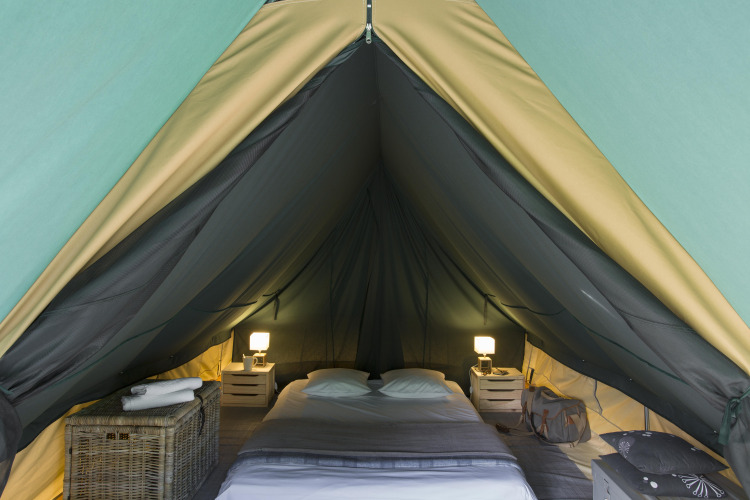 Vista interior de una tienda tipi acogedora con cama doble y mesitas en Village Huttopia Lac de Rillé, Francia.