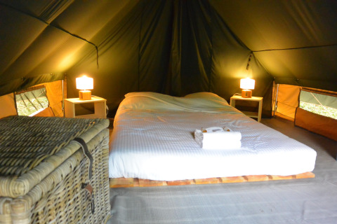 Acogedor espacio para dormir dentro de una tienda tipi con cama doble, mesitas, lámparas y una cesta.