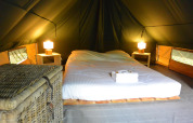 Acogedor espacio para dormir dentro de una tienda tipi con cama doble, mesitas, lámparas y una cesta.