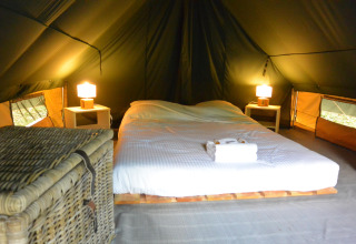 Acogedor espacio para dormir dentro de una tienda tipi con cama doble, mesitas, lámparas y una cesta.
