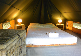 Acogedor espacio para dormir dentro de una tienda tipi con cama doble, mesitas, lámparas y una cesta.