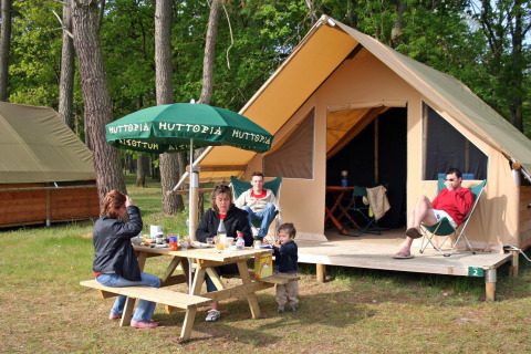 Familie frühstückt an einem Picknicktisch vor einem Safarizelt im Village Huttopia Lac de Rillé, Frankreich.