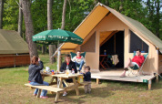Familia desayunando al aire libre junto a una tienda Canadienne en Village Huttopia Lac de Rillé, Francia.