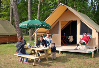 Familie frühstückt an einem Picknicktisch vor einem Safarizelt im Village Huttopia Lac de Rillé, Frankreich.