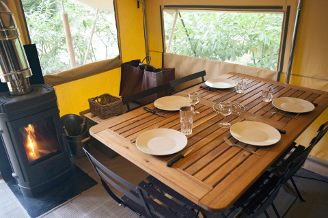 Mesa preparada para cuatro en tienda safari Trappeur con estufa de leña en Village Huttopia Lac de Rillé, Francia.